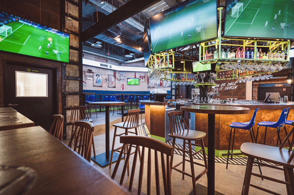 Ośmiokątny bar z telebimami, otoczony siedziskami przypominającymi trybuny dla widzów, fot. Aleksandra Miszkurka